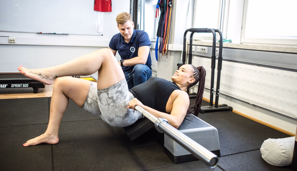 Fysioterapeutti ohjaa asiakasta lonkannostoharjoituksessa tangon kanssa