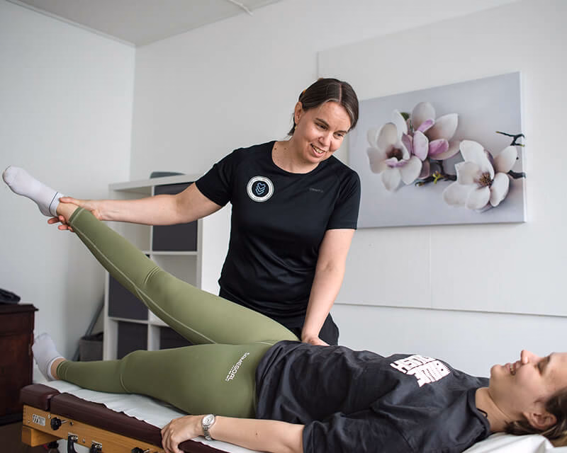 Fysioterapeutti Anne Leikas ohjaa asiakkaan jalan venytystä hoitopöydällä